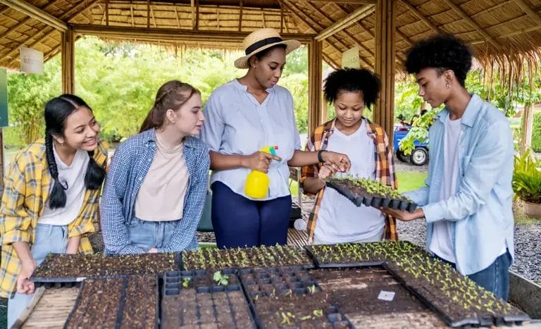 A female homeschool teacher instructs four teenage students in an outdoor gardening class.