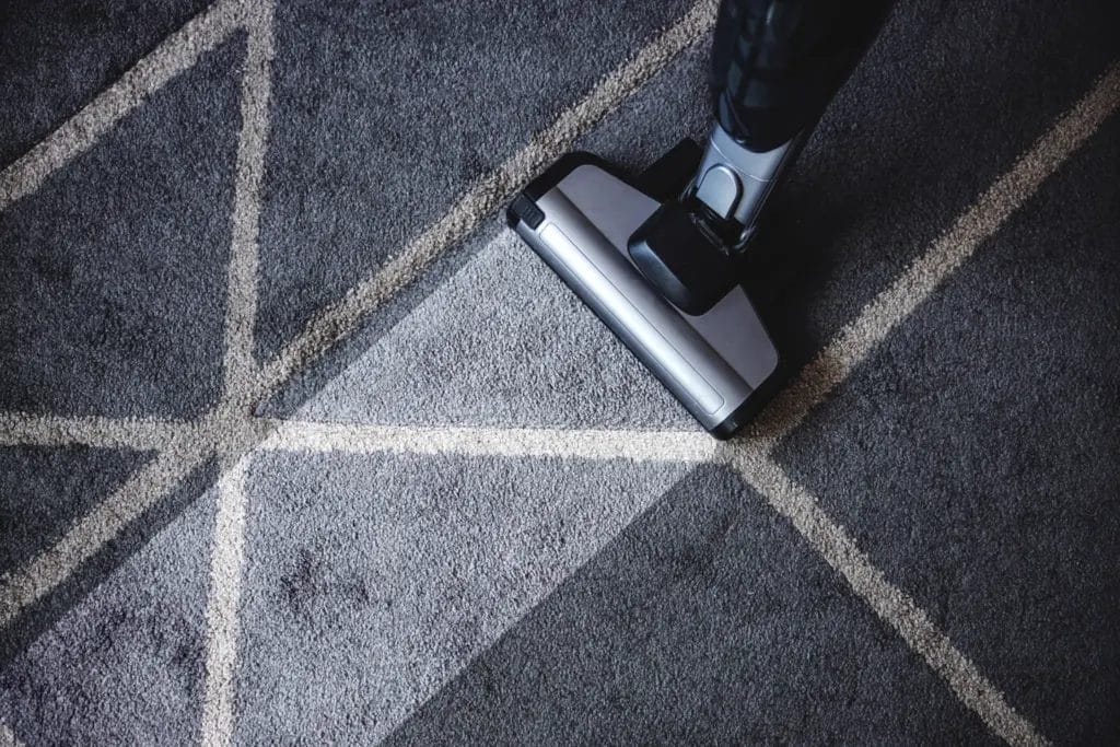 Close-up of an extractor machine cleaning a gray geometric rug.