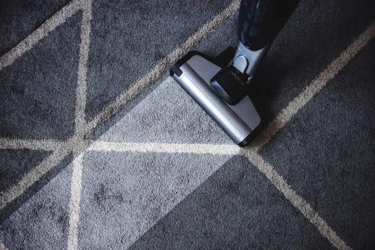 Close-up of an extractor machine cleaning a gray geometric rug.