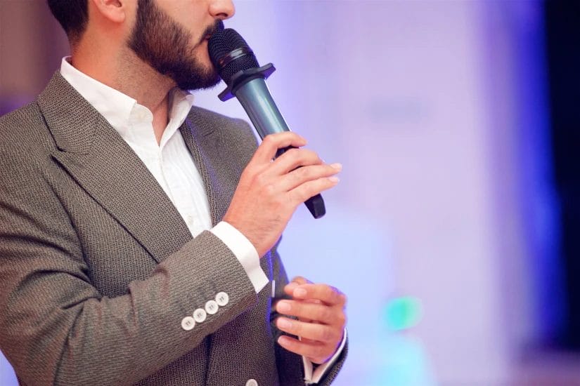 a close-up of a young male event host speaking into a microphone on stage