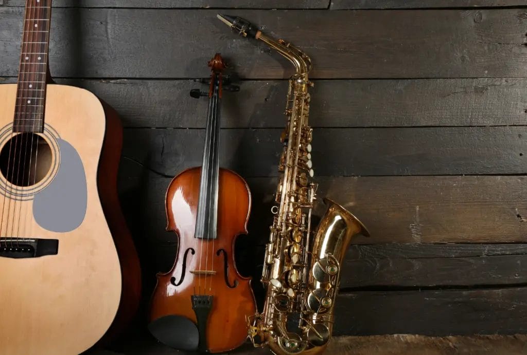 A guitar, saxaphone and violin, stood up against a dark wood backdrop