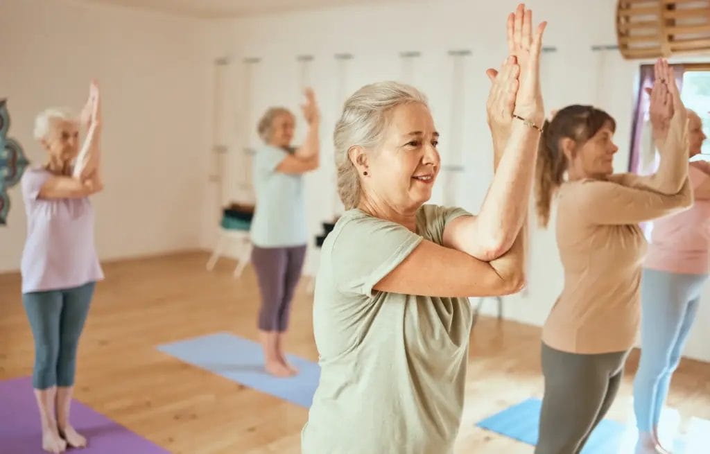 Women in pastel workout clothes practice eagle arms standing on yoga mats in a yoga class.