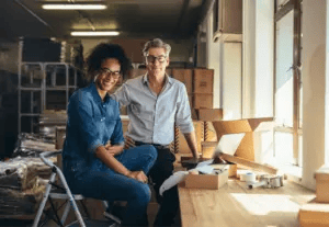 Online business owner smiles to the camera while packaging products in a warehouse.