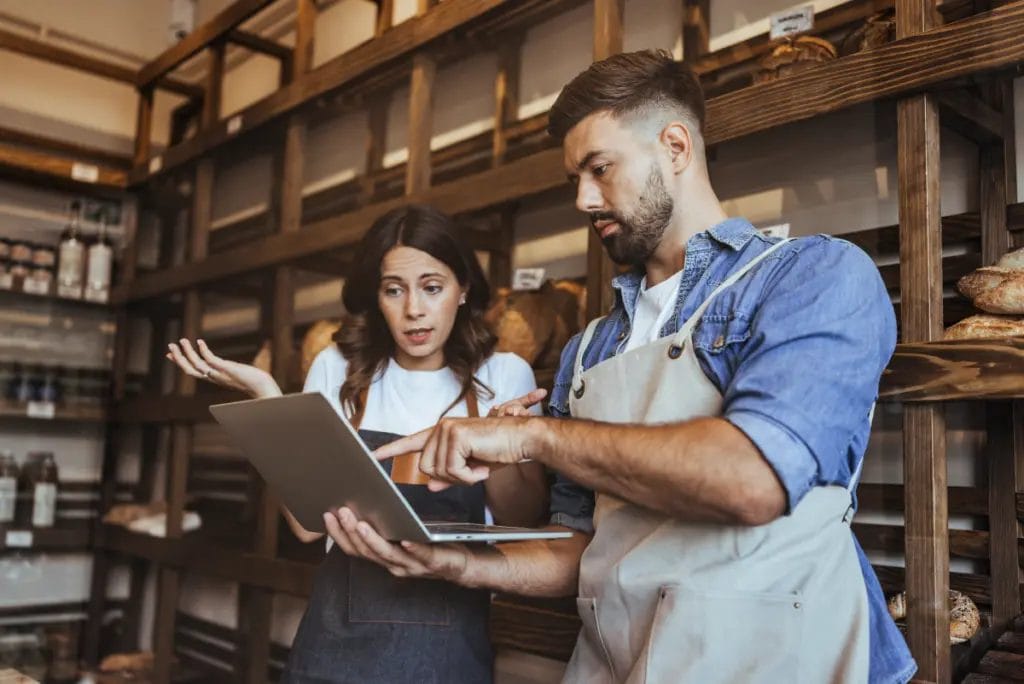 Two business owners in a storeroom troubleshoot a problem on a laptop