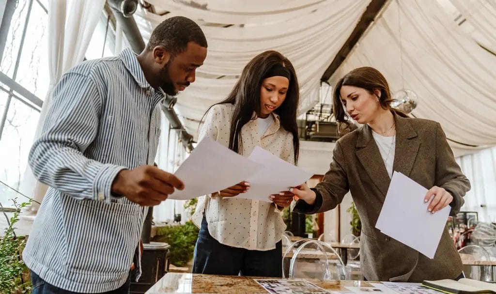 A party planner points to paperwork and plans a couple is holding as they discuss potential ideas for an upcoming event.