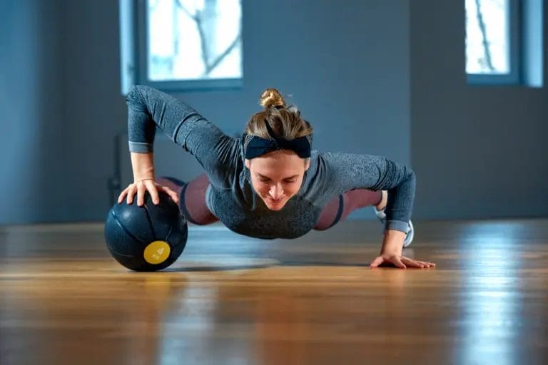 Fitness instructor performing wide-stance medicine ball push ups.