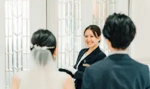 A wedding planner smiles at a bride and groom before she opens the door to their ceremony where they'll walk down the aisle.