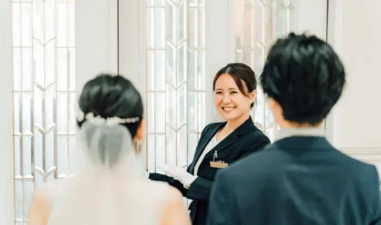 A wedding planner smiles at a bride and groom before she opens the door to their ceremony where they'll walk down the aisle.