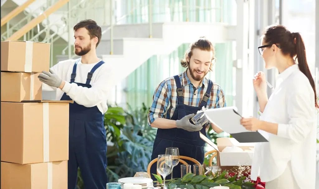 An event planner signs paperwork for a delivery worker as him and his team drop off boxes at a decorated indoor event venue before a big party.