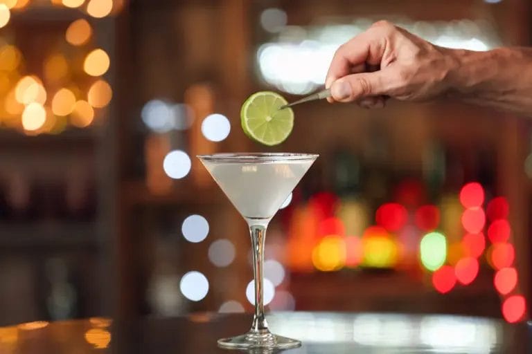 A bartender garnishes a cocktail with a slice of lime.