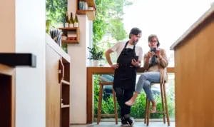 A business owner goes over digital contract information with a landlord as they both look at smartphones together in a cafe.