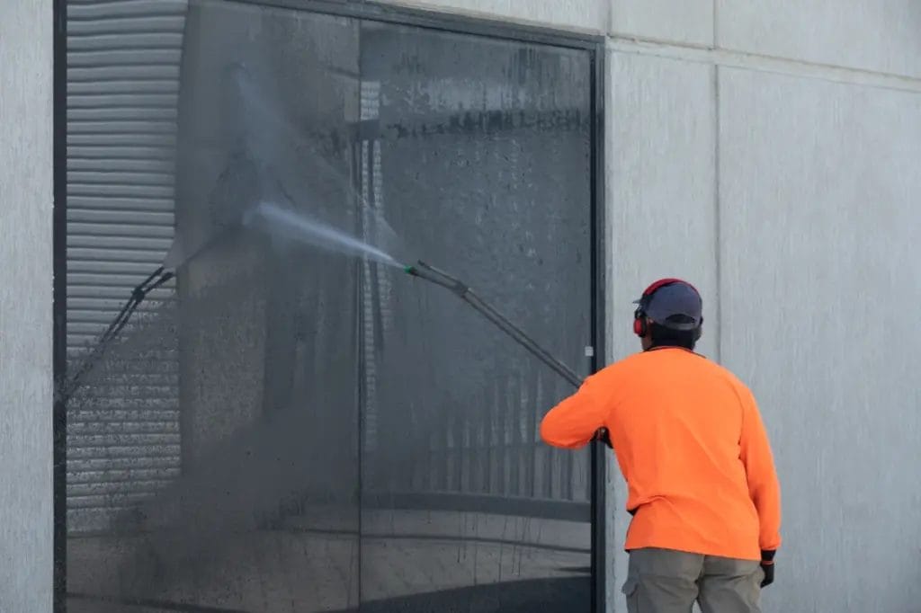 employee of a pressure washing business cleaning a large window