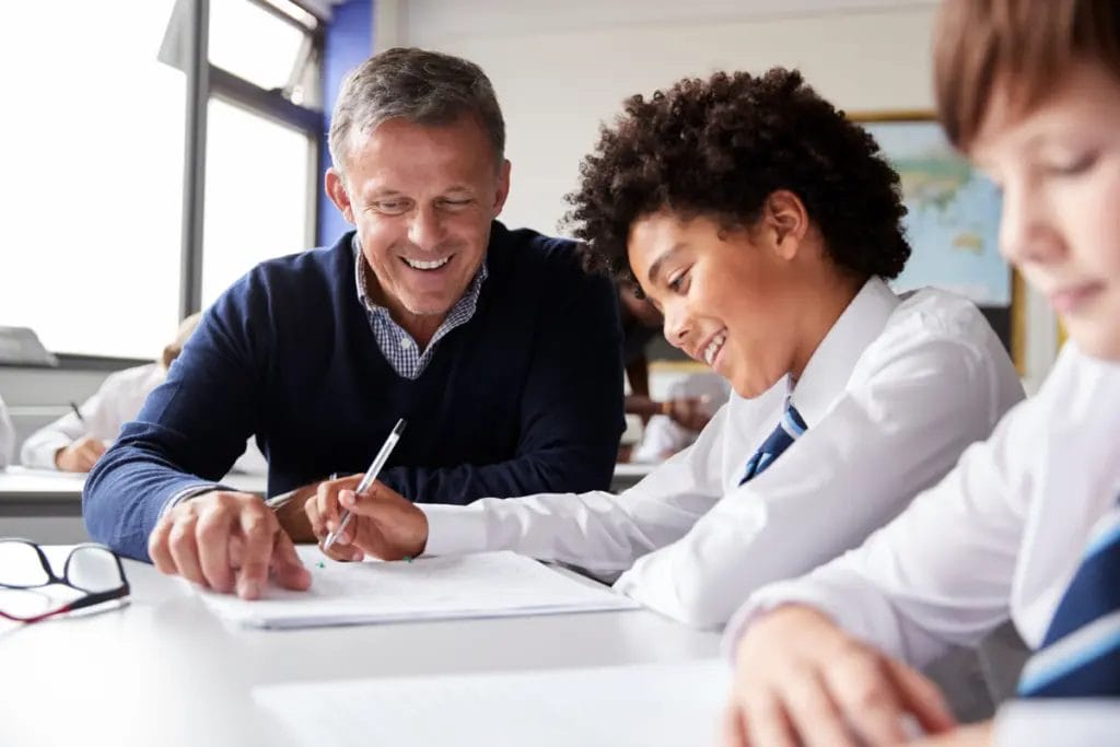 Private school teacher helps middle grade student with a worksheet in a bright, airy classroom.