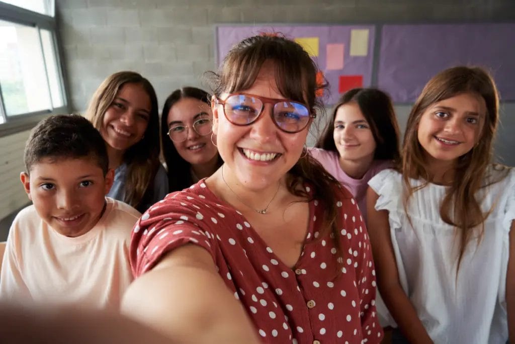 Teacher takes a smiling selfie with students in a small classroom