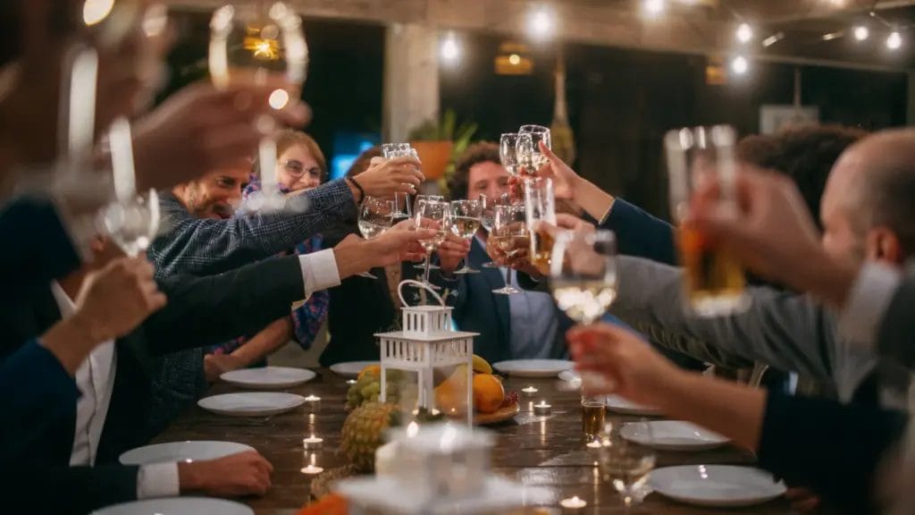 a group of event attendees in suits toasting glasses of wine while seated at a dinner table