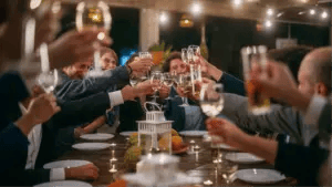 a group of event attendees in suits toasting glasses of wine while seated at a dinner table