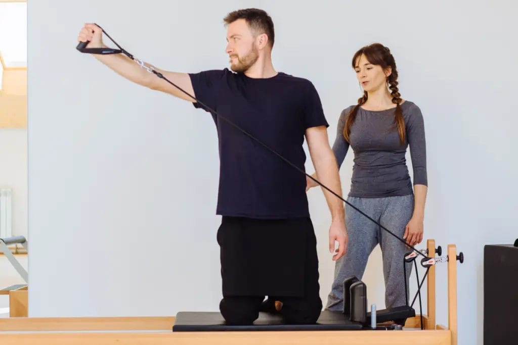 A Pilates instructor observes a student on a reformer.