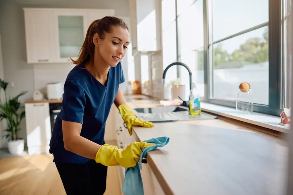 a young female housekeeper wearing protective gloves while cleaning a kitchen counter