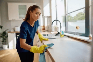 a young female housekeeper wearing protective gloves while cleaning a kitchen counter