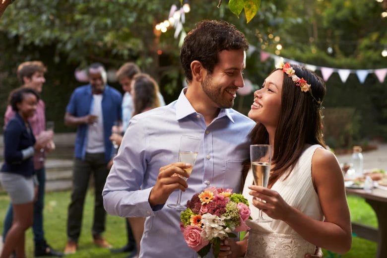 young couple holding champagne glasses celebrating a wedding in a backyard