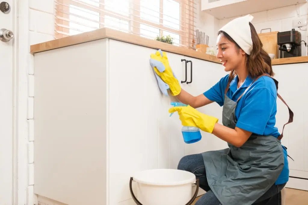 a house cleaner spraying and wiping off a kitchen cabinet