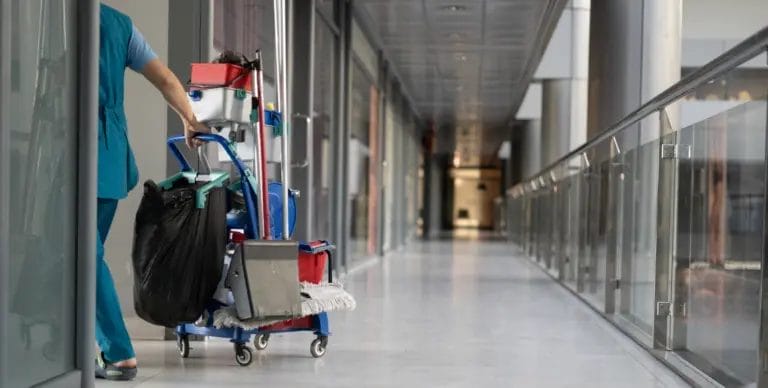 a janitor pulls a cleaning cart down an office hallway