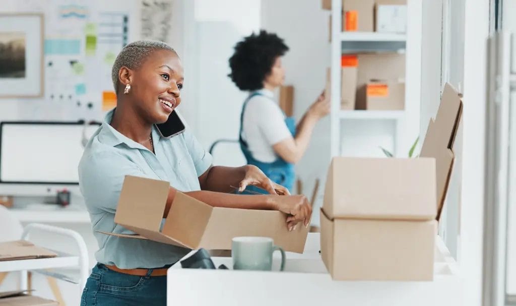 A businesswoman speaking on the phone while assembling boxes for shipping products to customers.