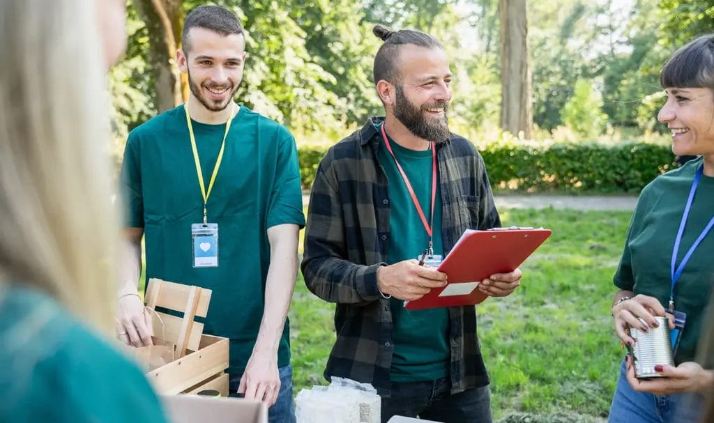 A group of employees eagerly listen to a manger who is reading off guidelines and instructions from a clipboard at an outdoor event.