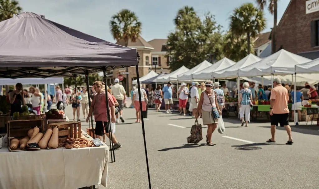 A busy outdoor farmers market is lined with vendors under pop-up tents selling fresh produce and handmade goods.