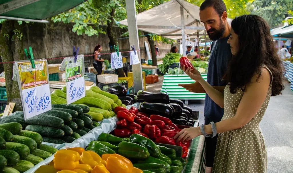 A couple browses a selection of fresh peppers on display at an outdoor farmers market.