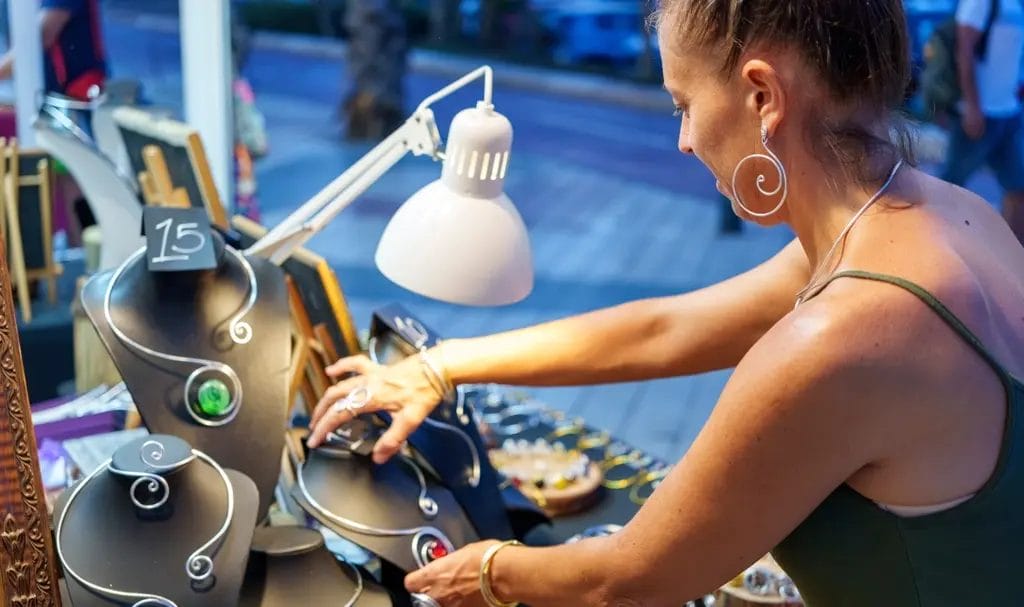 A jeweler organizes the display of her handmade jewelry in her booth at an outdoor market.