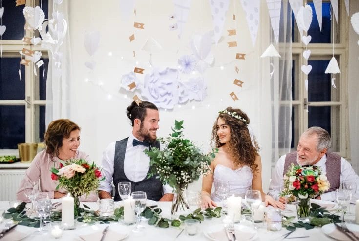 a young bride and groom sitting at a table between parents looking at each other