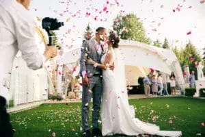 photographer taking picture of bride and groom kissing among rose petals