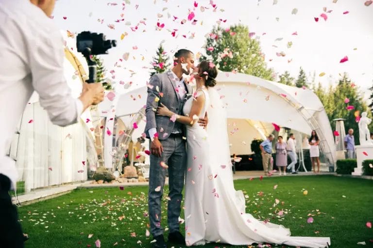 photographer taking picture of bride and groom kissing among rose petals