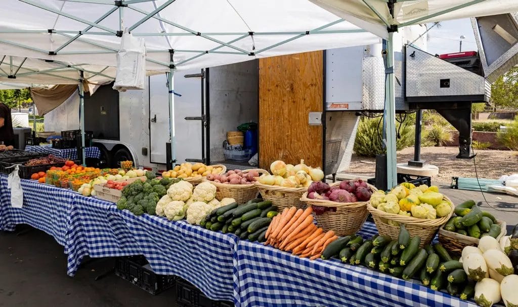 A vendor has various fresh vegetables on display under a shady tent.