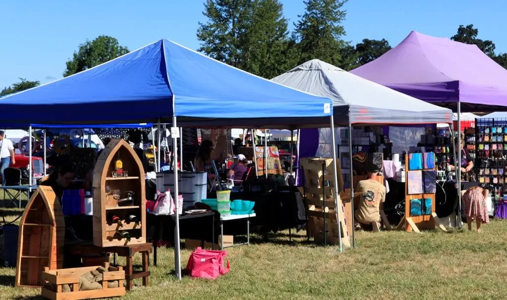 Handmade products on display under blue and purple pop-up tents at an outdoor event.