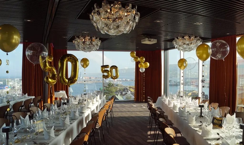 A banquet hall with set tables and balloons, decorated for a 50th celebration.