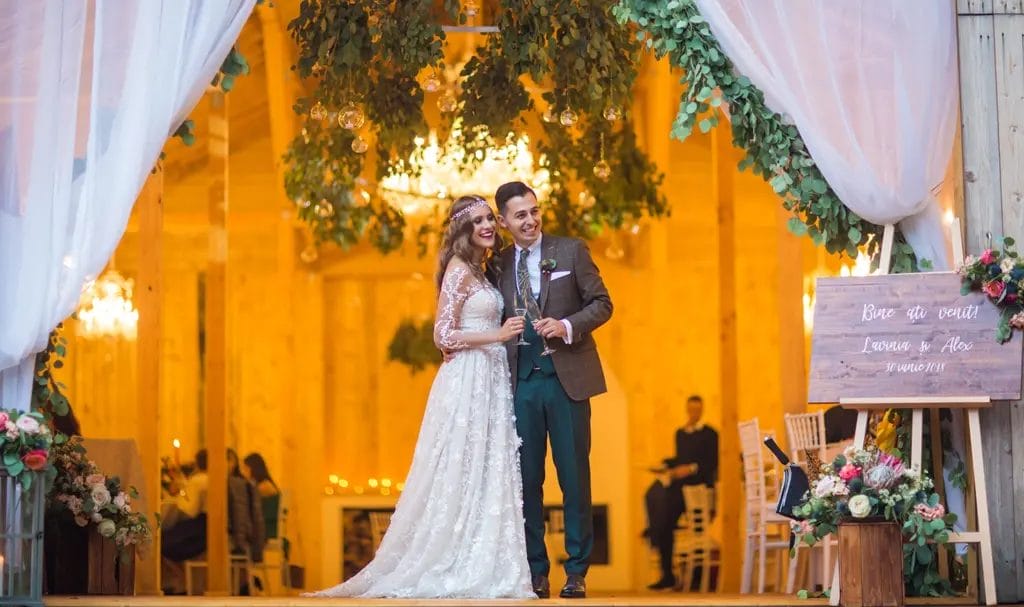 A newlywed bride and groom stand at the entrance to their wedding reception, happily toasting to their ceremonious day.