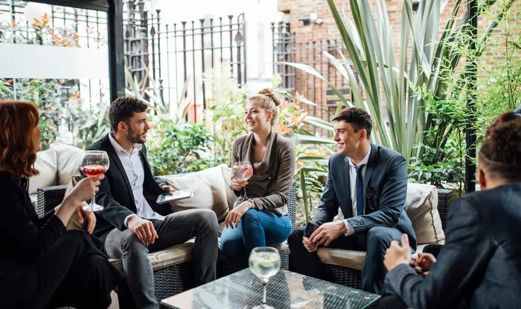 A group happily chats and smiles while enjoying drinks on an outdoor patio of an event venue.