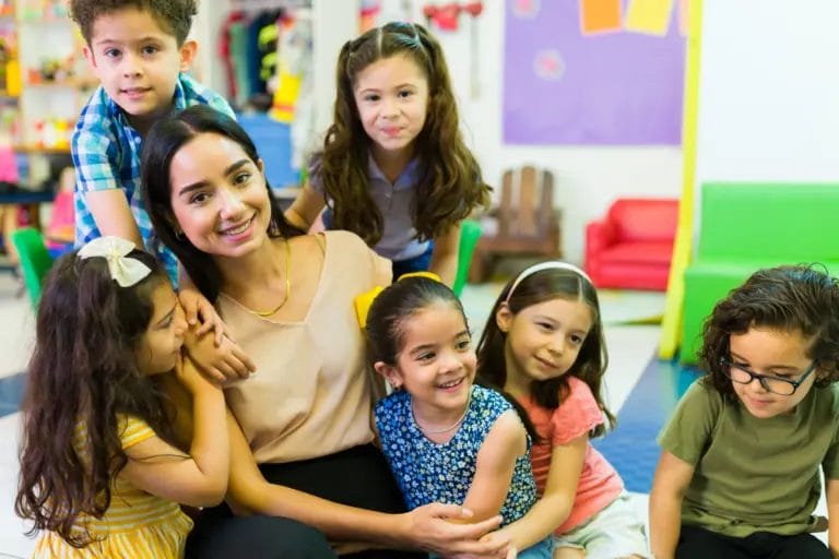 teacher with young students surrounding her in classroom smiling