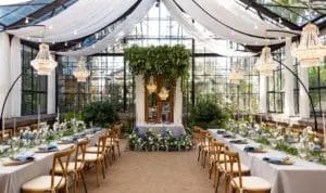 A wedding venue set up for a reception, with chandeliers hanging over decorated dining tables.