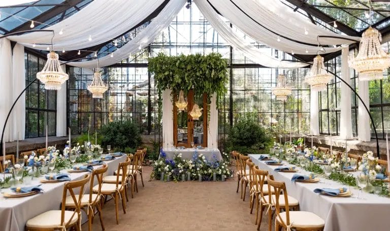 A wedding venue set up for a reception, with chandeliers hanging over decorated dining tables.