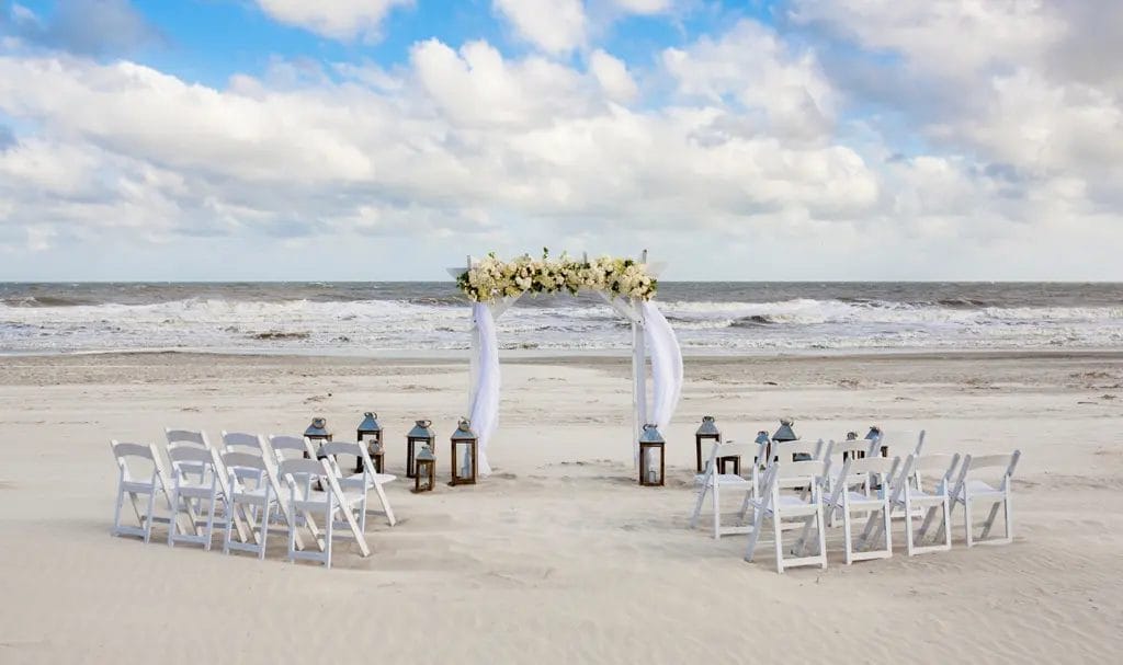 An altar, lanterns, and chairs are prepped for a wedding ceremony on a beach.
