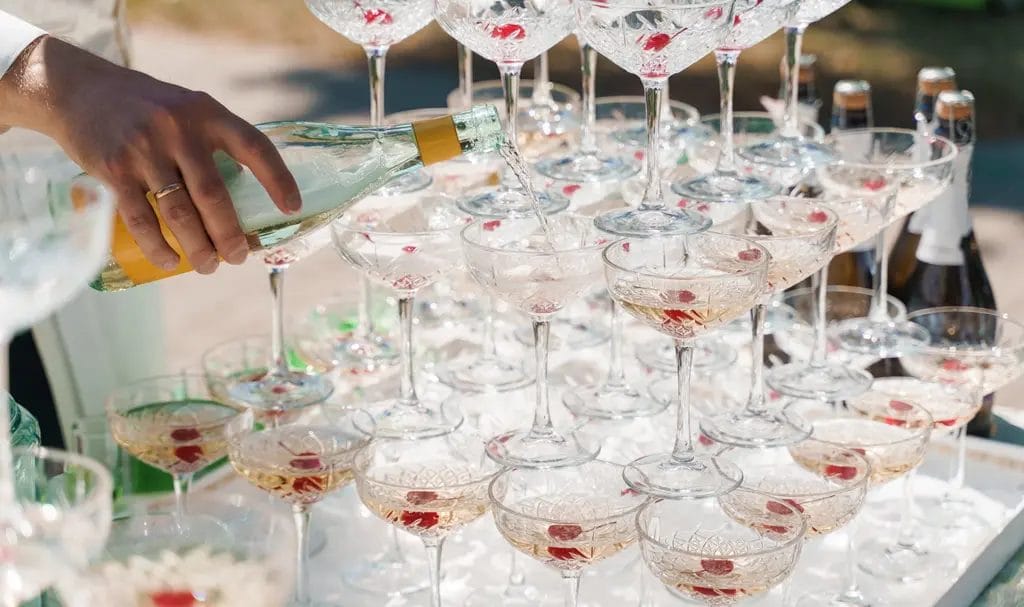 A bartender pours champagne into a tower of glasses.