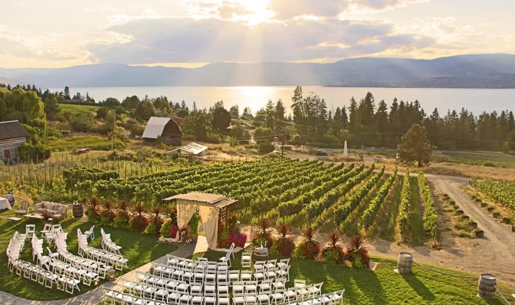 A panoramic view of a winery with chairs and an altar staged for a late afternoon wedding ceremony.