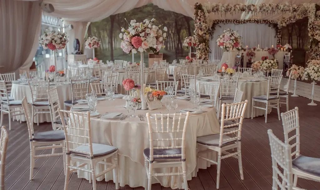 Indoor wedding venue ballroom with fabric draped on the ceilings and walls, and tables set for a reception.