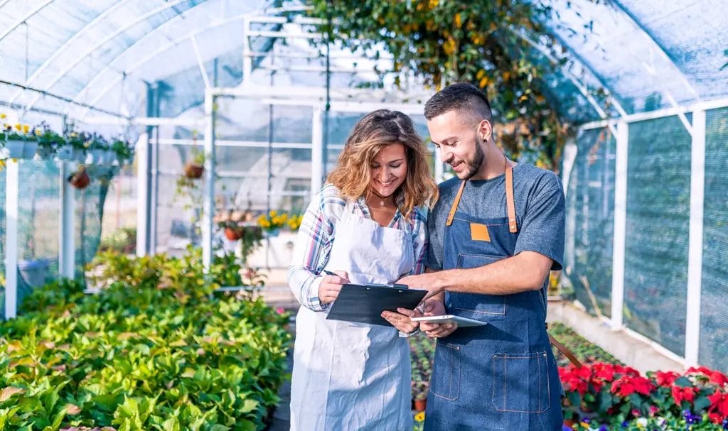 A small business owner reviews contract paperwork with another business owner in a greenhouse garden.