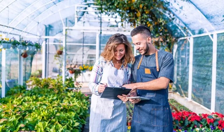A small business owner reviews contract paperwork with another business owner in a greenhouse garden.