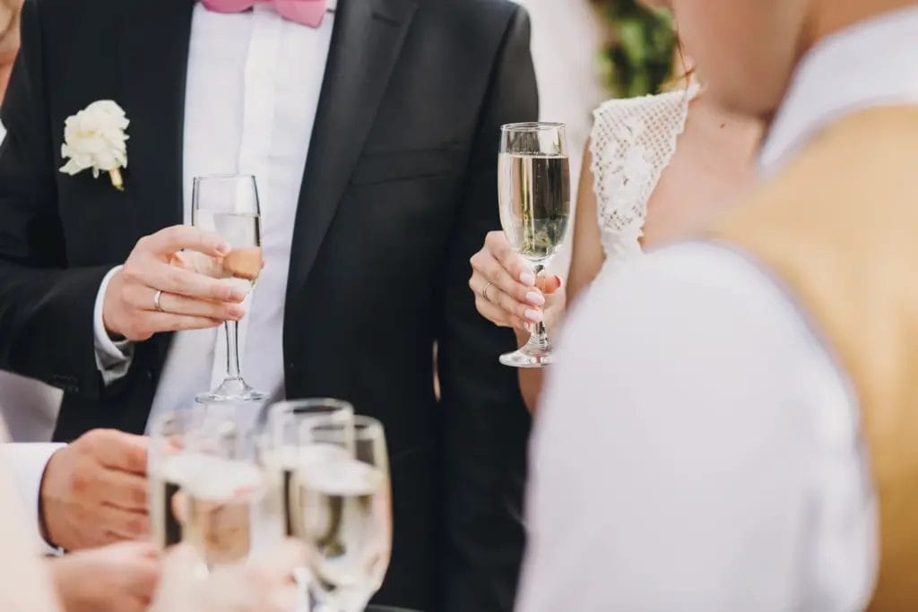 a close up of a bride and groom holding champagne glasses next to a server