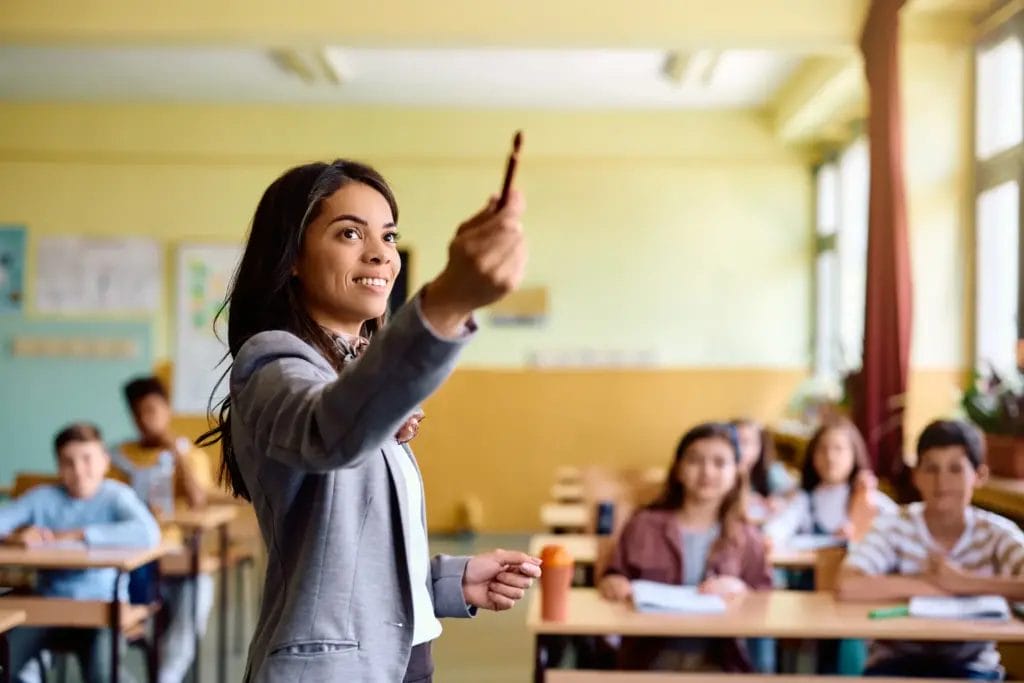 Teacher points to the board in front of a middle-grade classroom
